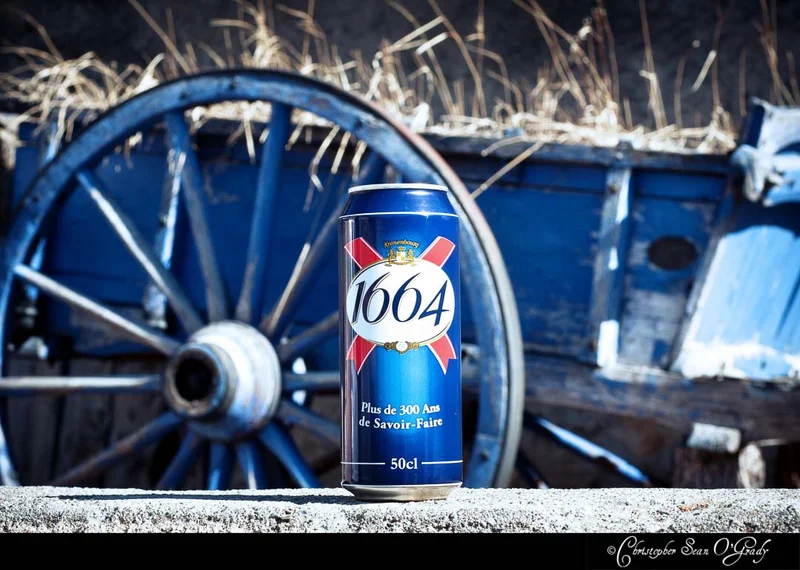 Kronenbourg 1664 beer can in front of a rustic blue wooden cart wheel