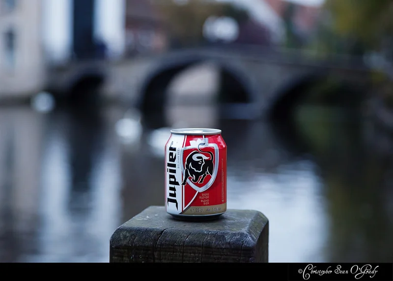 Jupiler Belgian beer can on a wooden post by a canal with stone bridge