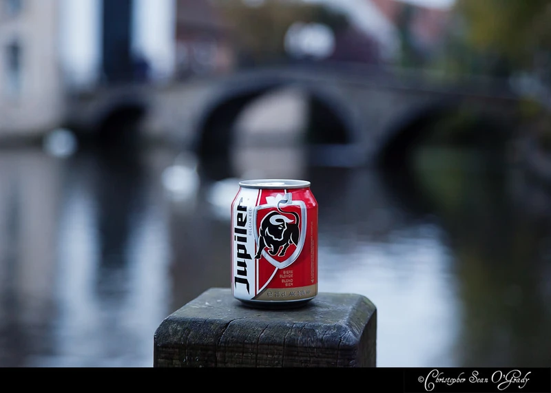 Jupiler Belgian beer can on a wooden post by a canal with stone bridge