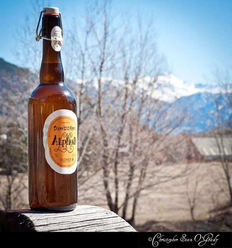 Alphand Blonde beer bottle on wooden ledge with snowy French Alps behind