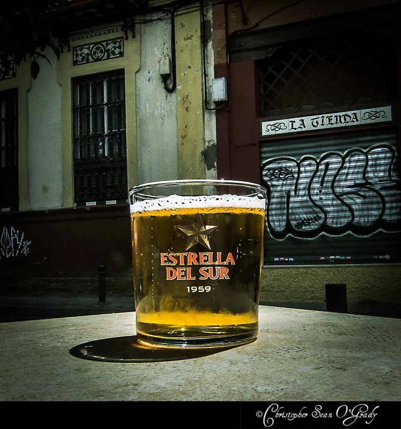 Estrella del Sur beer in branded glass at a Spanish sidewalk cafe with graffiti