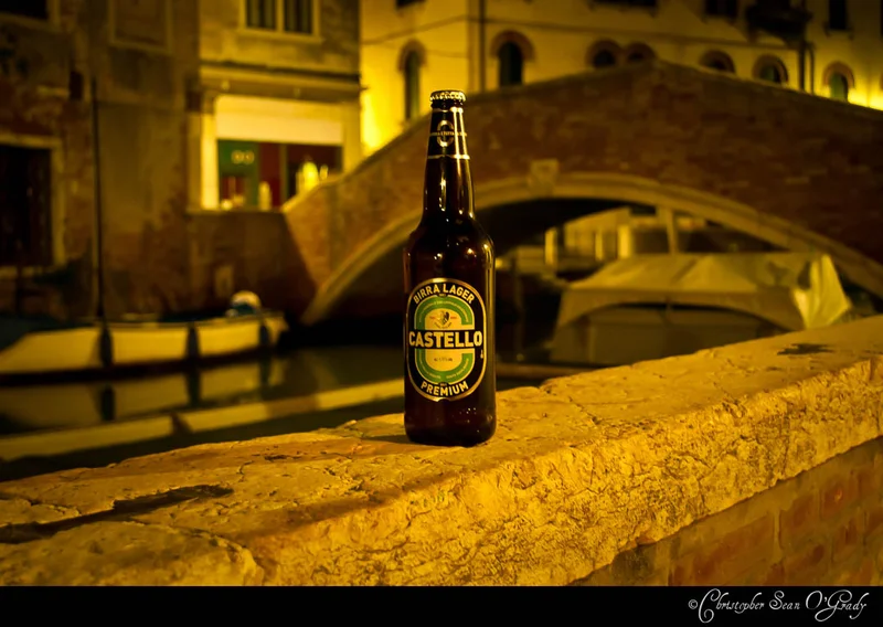 Castello Premium Birra Lager on a stone wall at a Venice canal at night