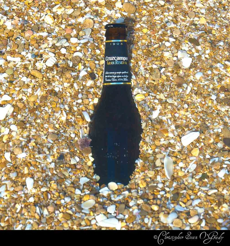 Cruzcampo Gran Reserva beer bottle on a pebble and shell beach