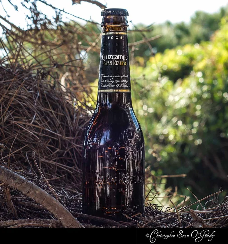 Cruzcampo Gran Reserva beer bottle with dry branches and green foliage