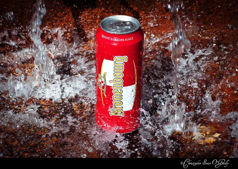 Kronenbourg can with water splashing around it on a dark surface