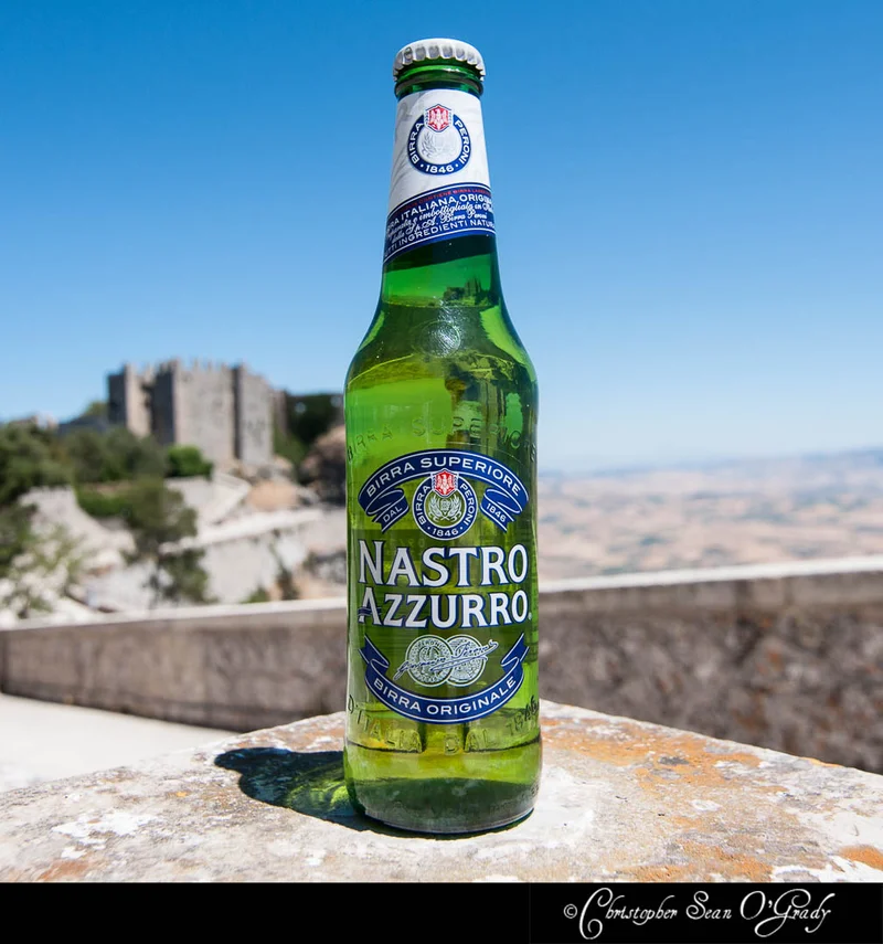 Nastro Azzurro beer bottle on a stone ledge with hilltop castle and valley view