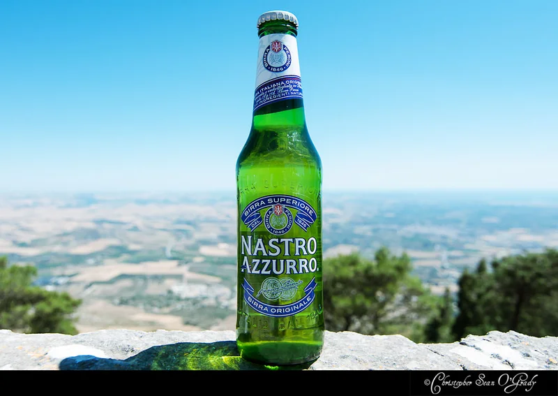 Nastro Azzurro beer bottle on a stone wall overlooking panoramic countryside