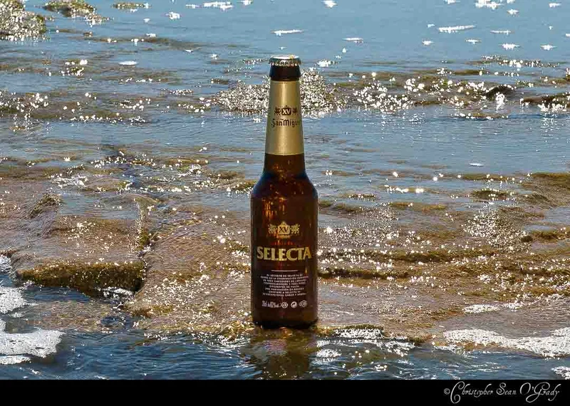 San Miguel Selecta beer bottle standing in shallow sparkling tidal water