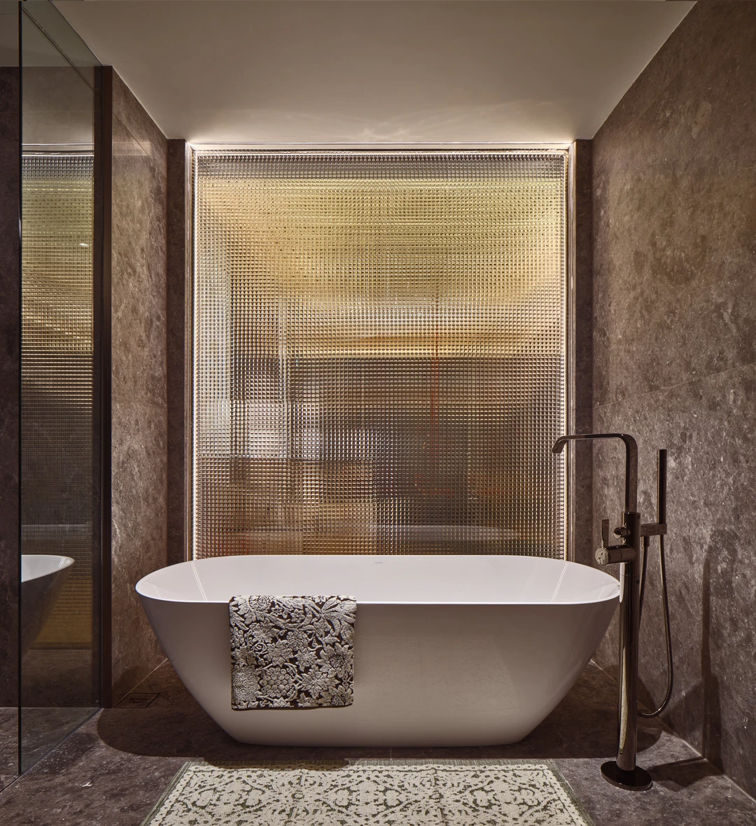 W Residences 5-bedroom showflat bathroom with freestanding tub, dark stone walls and warm backlit shower glass