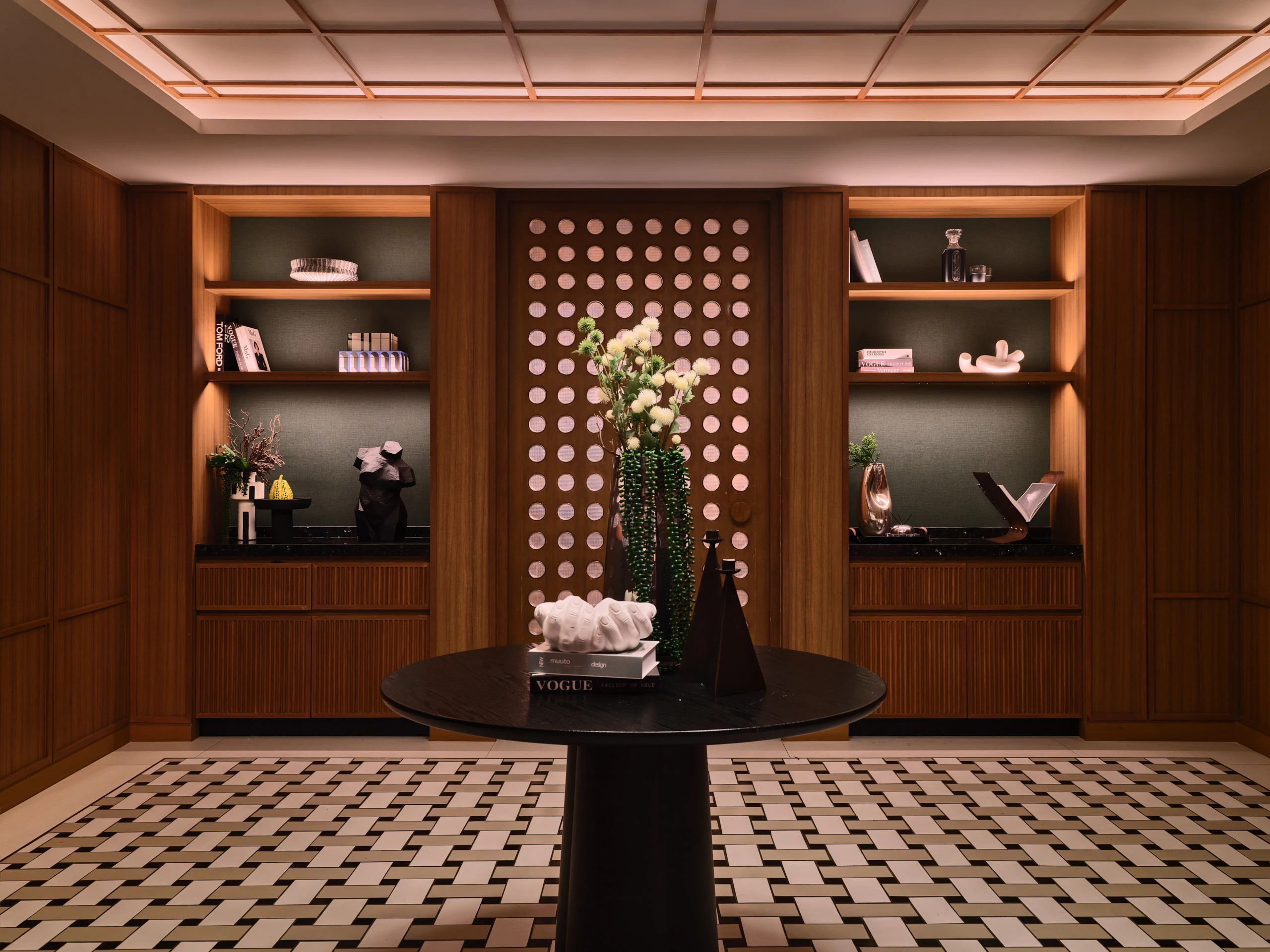 Foyer with round black table, white floral arrangement, perforated screen, geometric floor tiles, and built-in display shelves