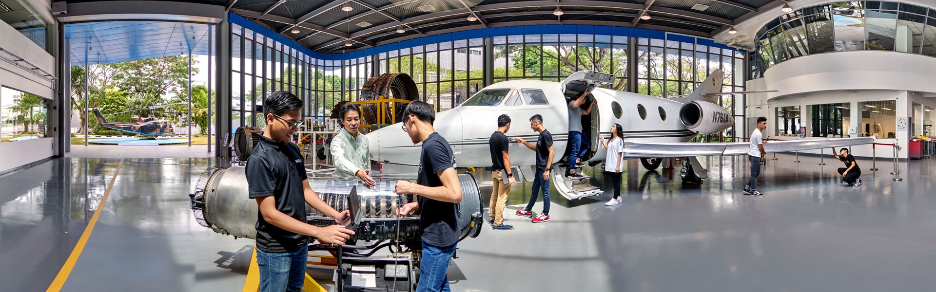 360 panorama of Ngee Ann Polytechnic aerospace hub with students inspecting a jet engine beside a private aircraft