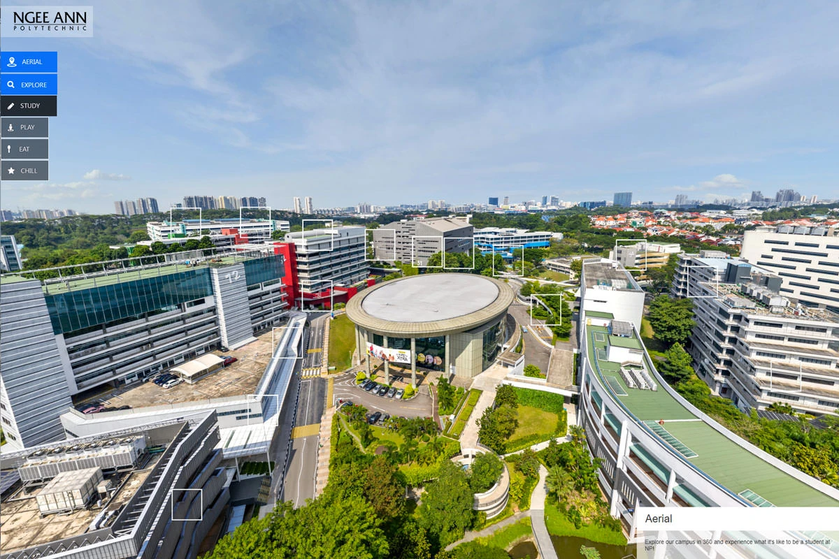 Aerial virtual tour view of a polytechnic campus with modern buildings, green rooftops, circular auditorium, navigation hotspots, and suburban skyline beyond.