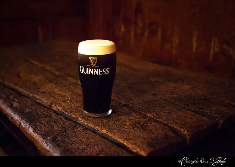 Guinness pint with creamy head on a rustic wooden table in a dimly lit pub