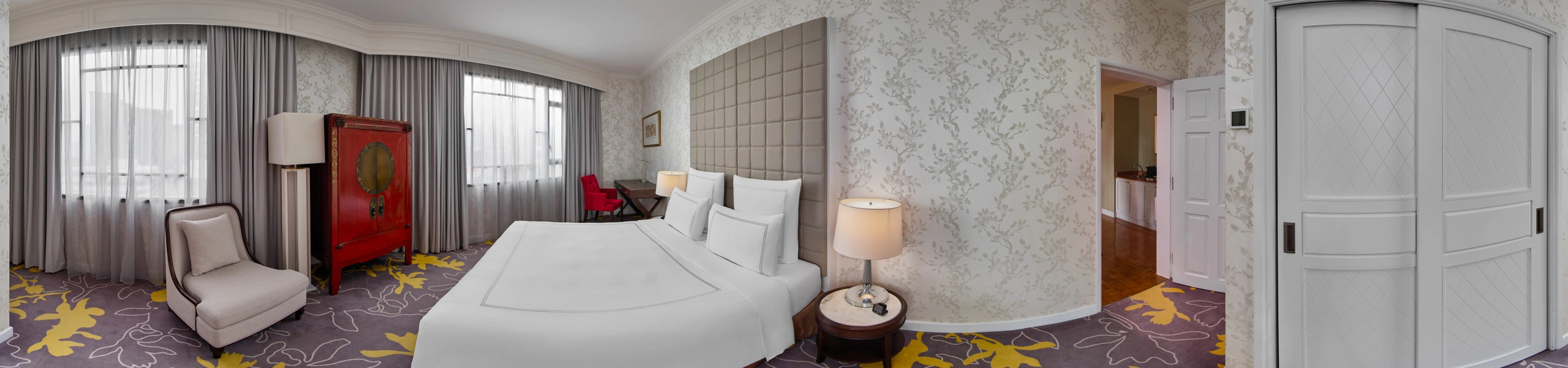 Paradox Singapore Emerald Suite bedroom panorama with white bed, grey tufted headboard, and red lacquered armoire