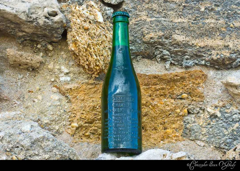 Alhambra Cerveza Extra green bottle resting against a weathered stone wall