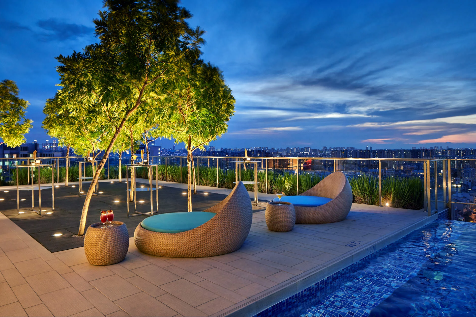 Rooftop pool deck with wicker loungers and city skyline at sunset