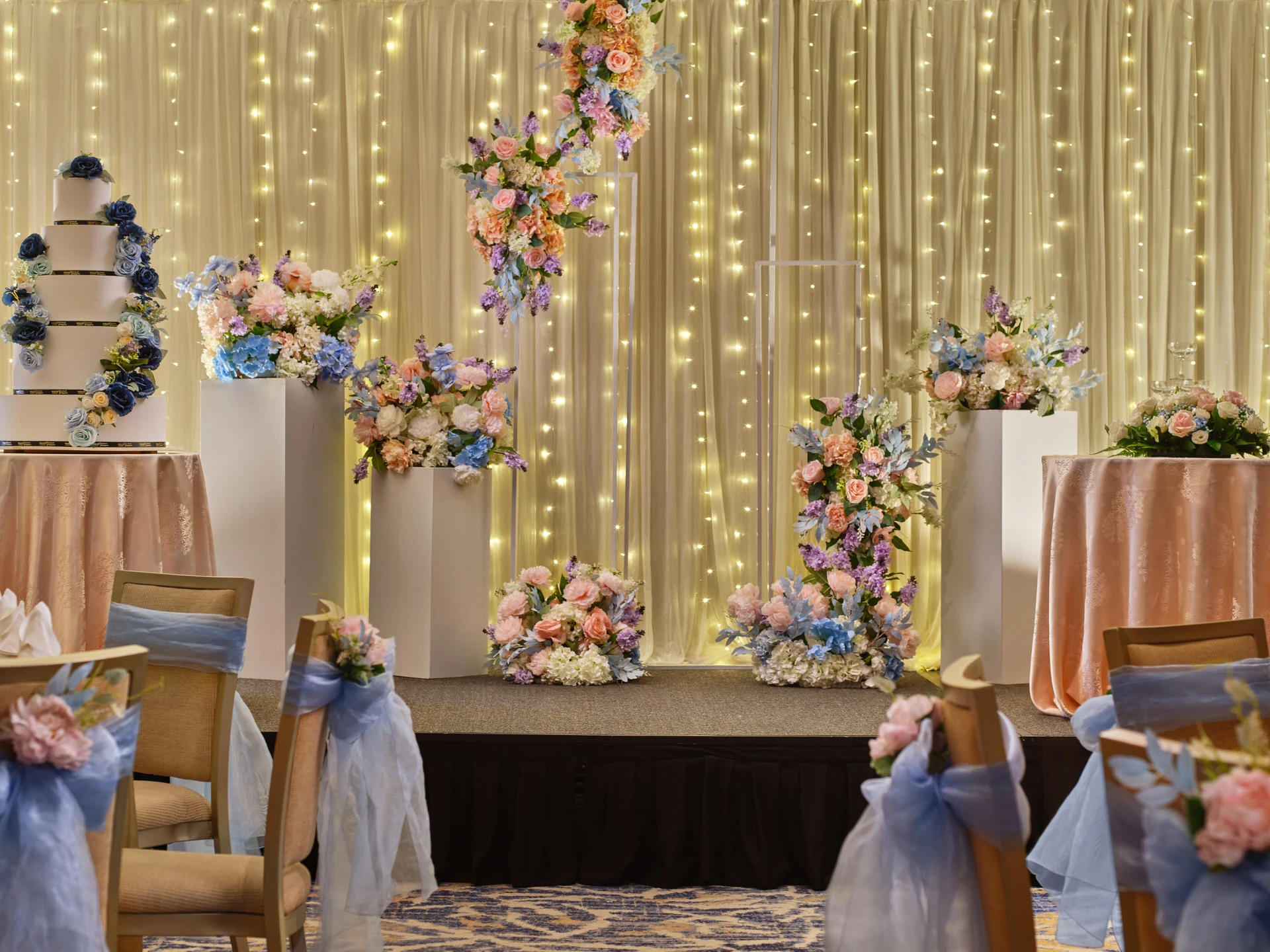 Wedding stage with fairy-light curtain, tiered cake and pastel floral plinths - voco Orchard Singapore event photography