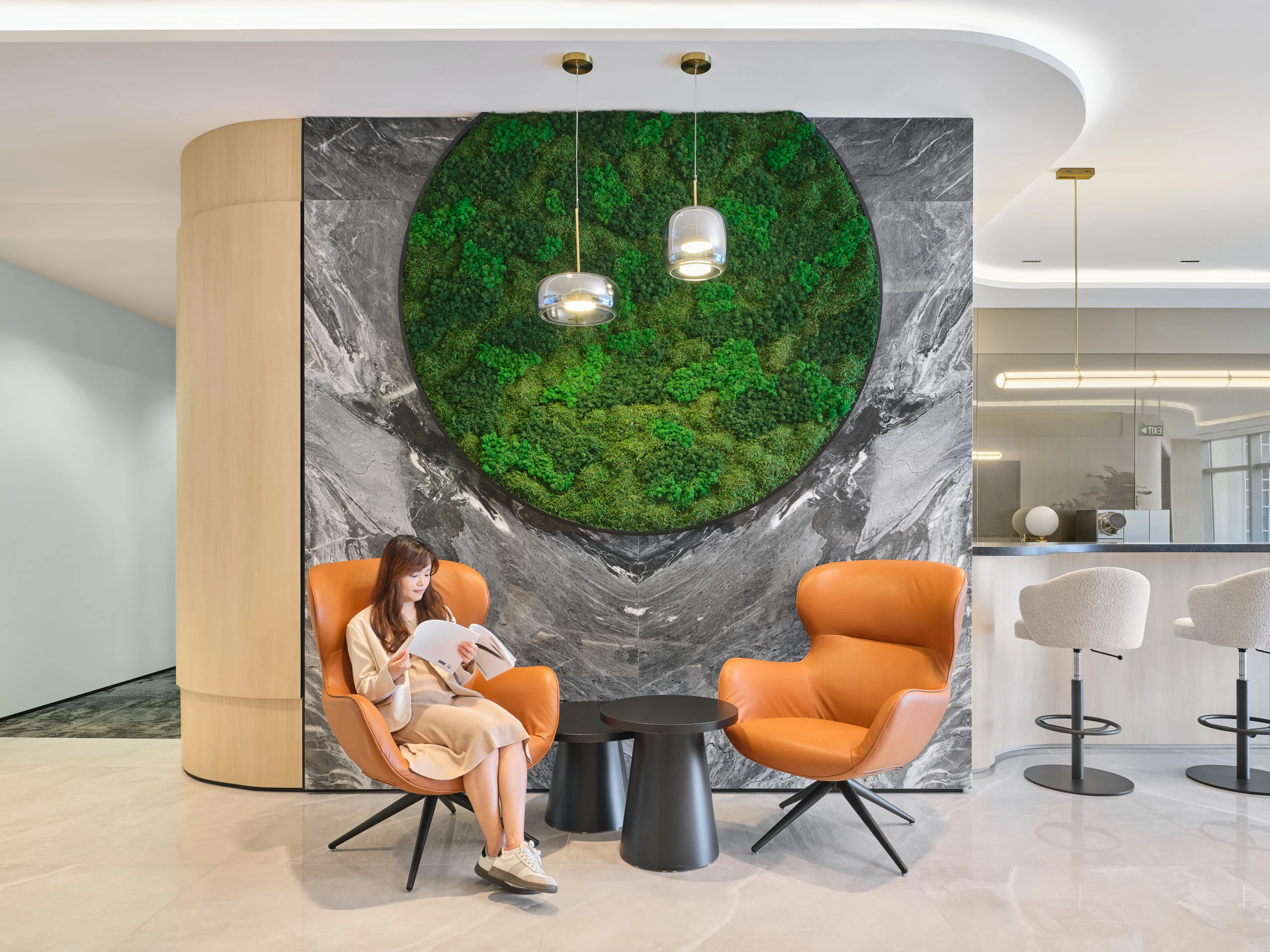 Reception detail with cognac wingback chairs and glass pendants beside moss wall