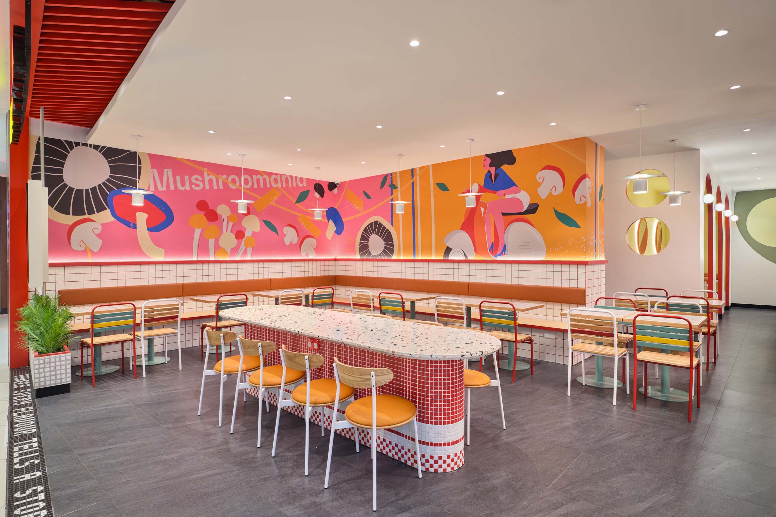 PastaMania Lot One seating area with Mushroomania mural, terrazzo communal table with red mosaic tile base, and banquette seating